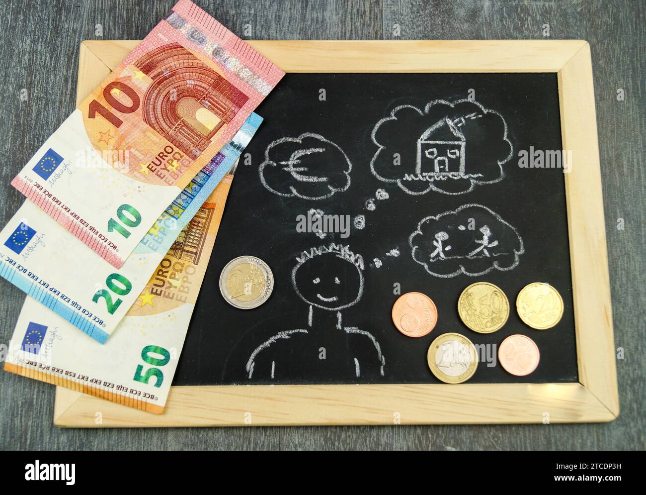 Ein Mann mit Gedankenblase, der "Euro, Haus, Kinder" auf ein Schiefer wirft, symbolisches Bild für den Aufbau von Kindergeld Stockfoto