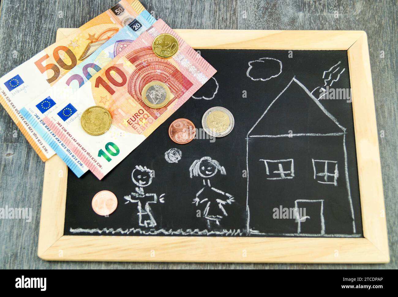 Geld auf Schiefer mit gezogenen Kindern und Haus, symbolisches Bild für den Aufbau von Kindergeld Stockfoto
