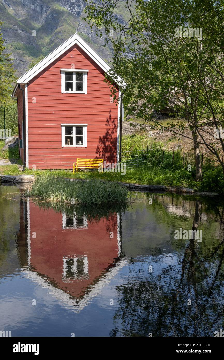 Altes rotes Holzhaus im Dorf Flåm, das sich in einem kleinen Teich spiegelt Stockfoto