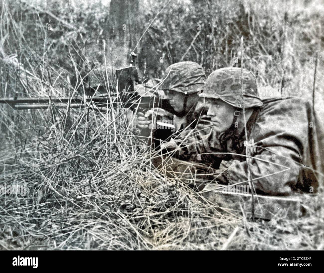 DEUTSCHE WAFFEN-SS-Soldaten feuern ein leichtes Maschinengewehr MG26 mit Tarnhelmen und Mänteln ab. Stockfoto