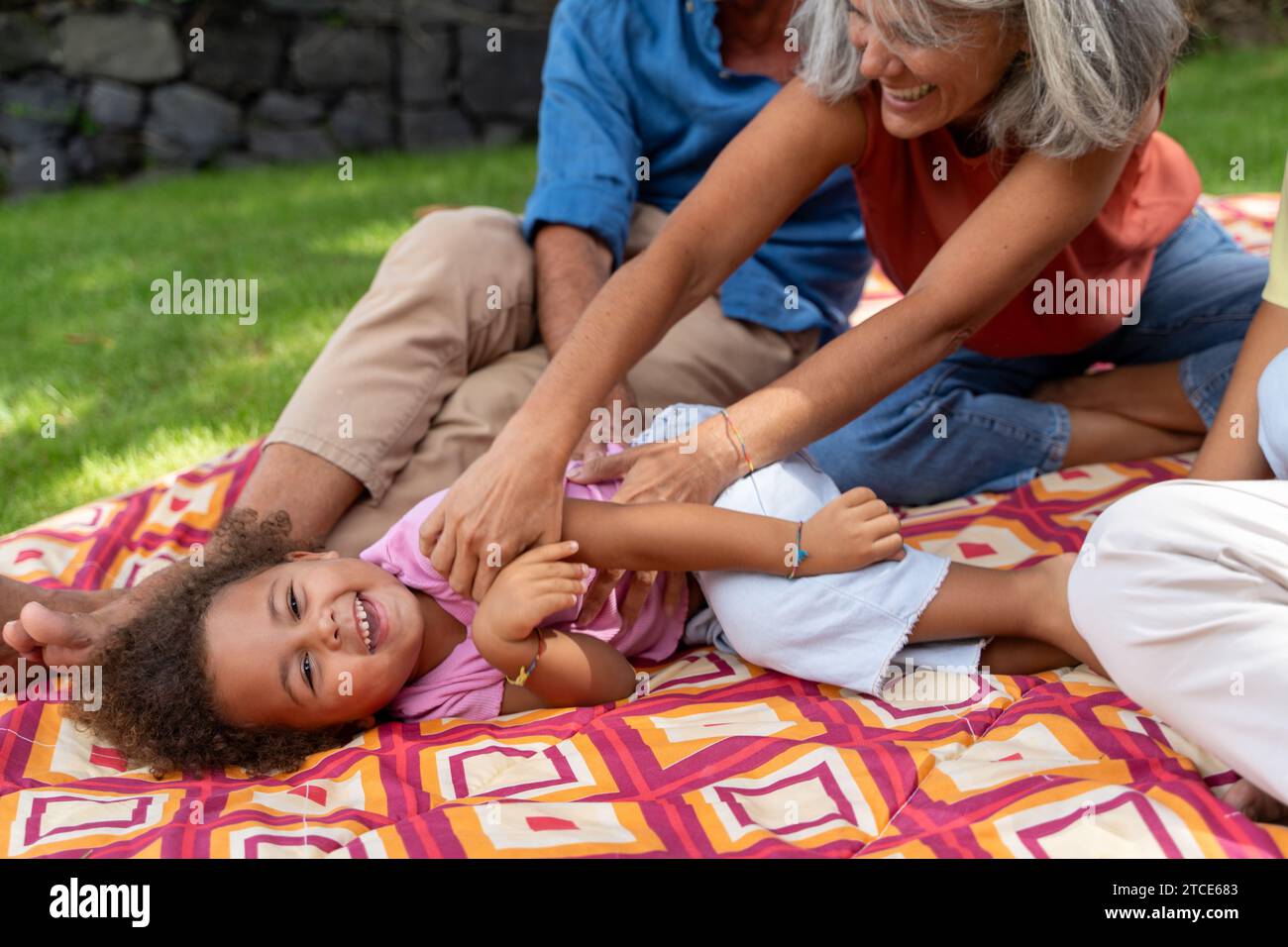 Ein junges Mädchen kichert, während ihre Großmutter sie während eines Familientages kitzelt und zeigt die Wärme einer interrassischen Familie. Stockfoto