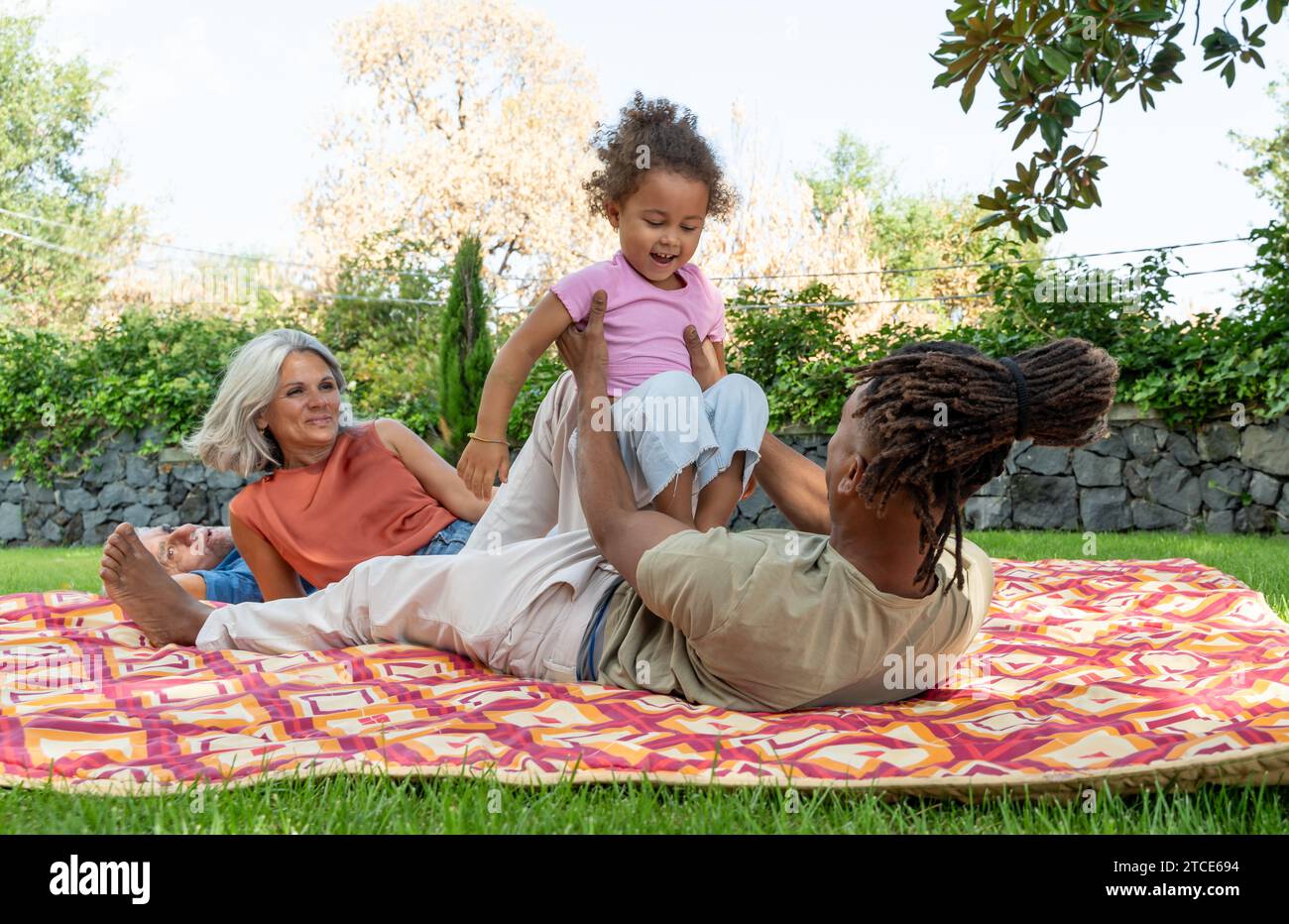 Ein verspielter Moment, in dem ein Vater sein Kleinkind in die Luft hebt, während anbetende Großeltern zusehen und die Einheit und das Glück der Familie reflektieren. Stockfoto