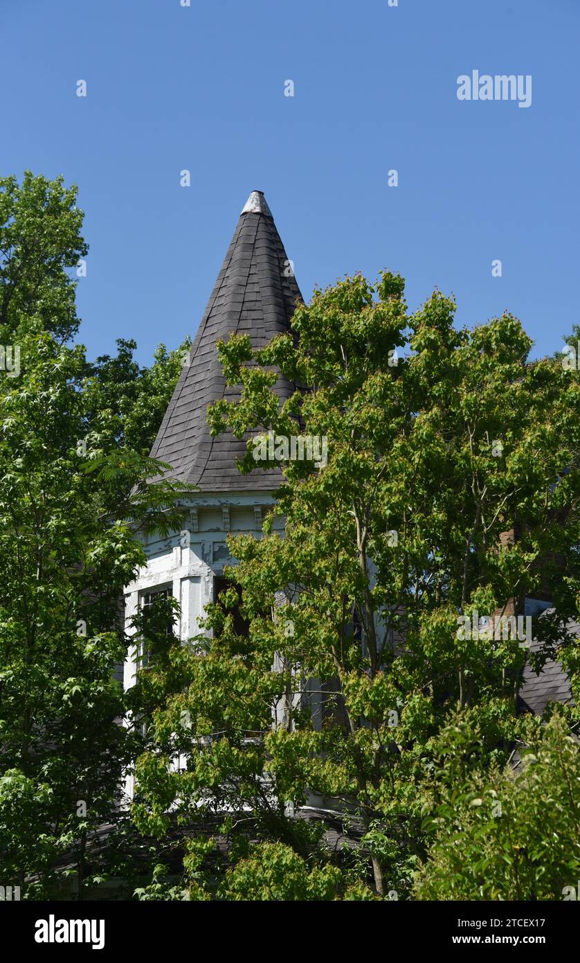 Altes, historisches, viktorianisches Haus wurde überwuchert und verlassen. Der runde Turm ist mit einer Zinnkappe und Schindeln gekrönt. Die Farbe ist rissig und blättert ab. Stockfoto