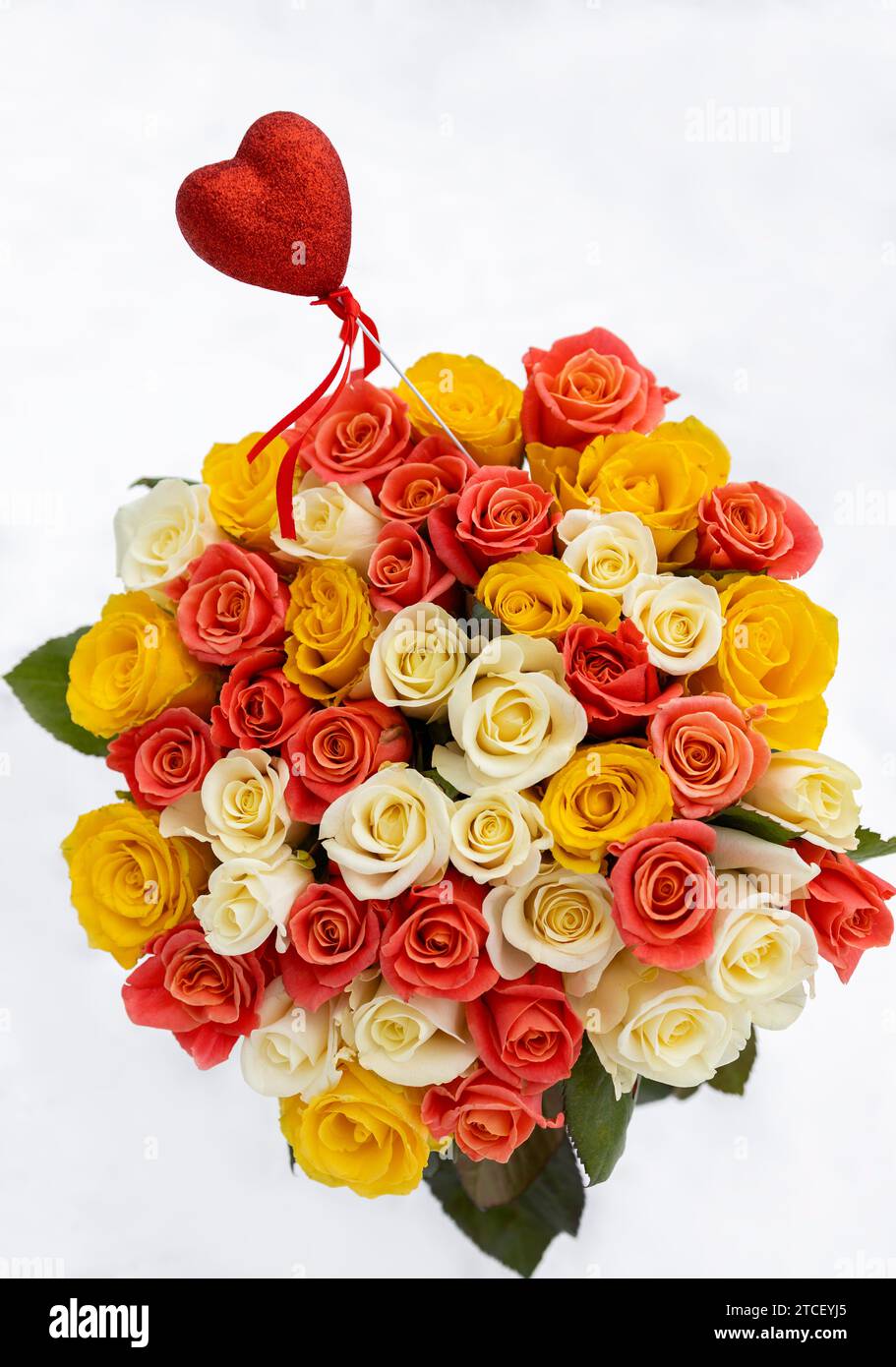 Buntes Blumenstrauß von Rosenblüten aus mehrfarbigen Rosen in drei Farben, auf weißem Schneehintergrund. Rotes Souvenir-Herz ragt aus einem Blumenstrauß hervor. Valen Stockfoto