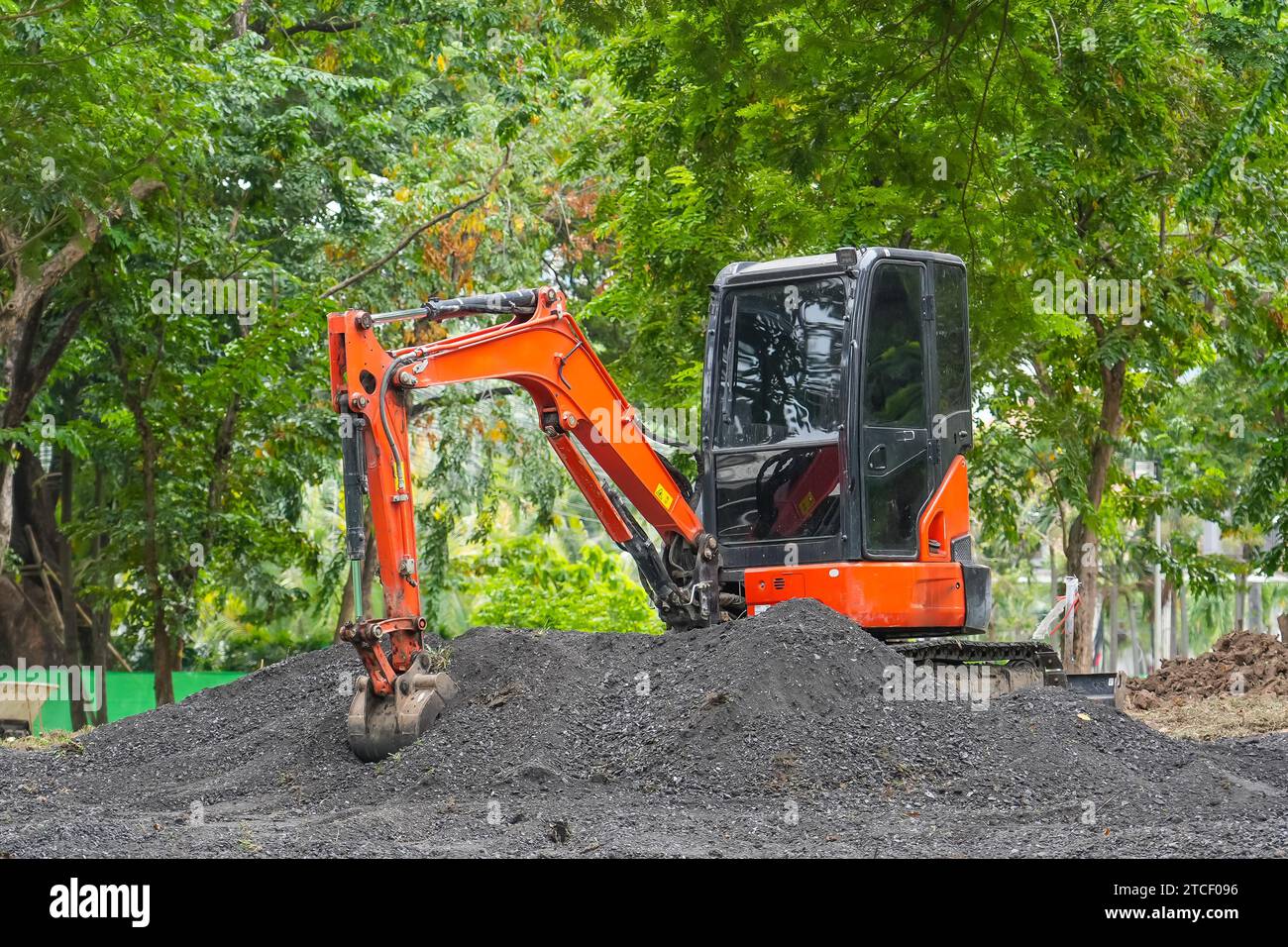 Der orangefarbene Minibagger im Betrieb gräbt und lädt fruchtbaren Boden im Park Stockfoto