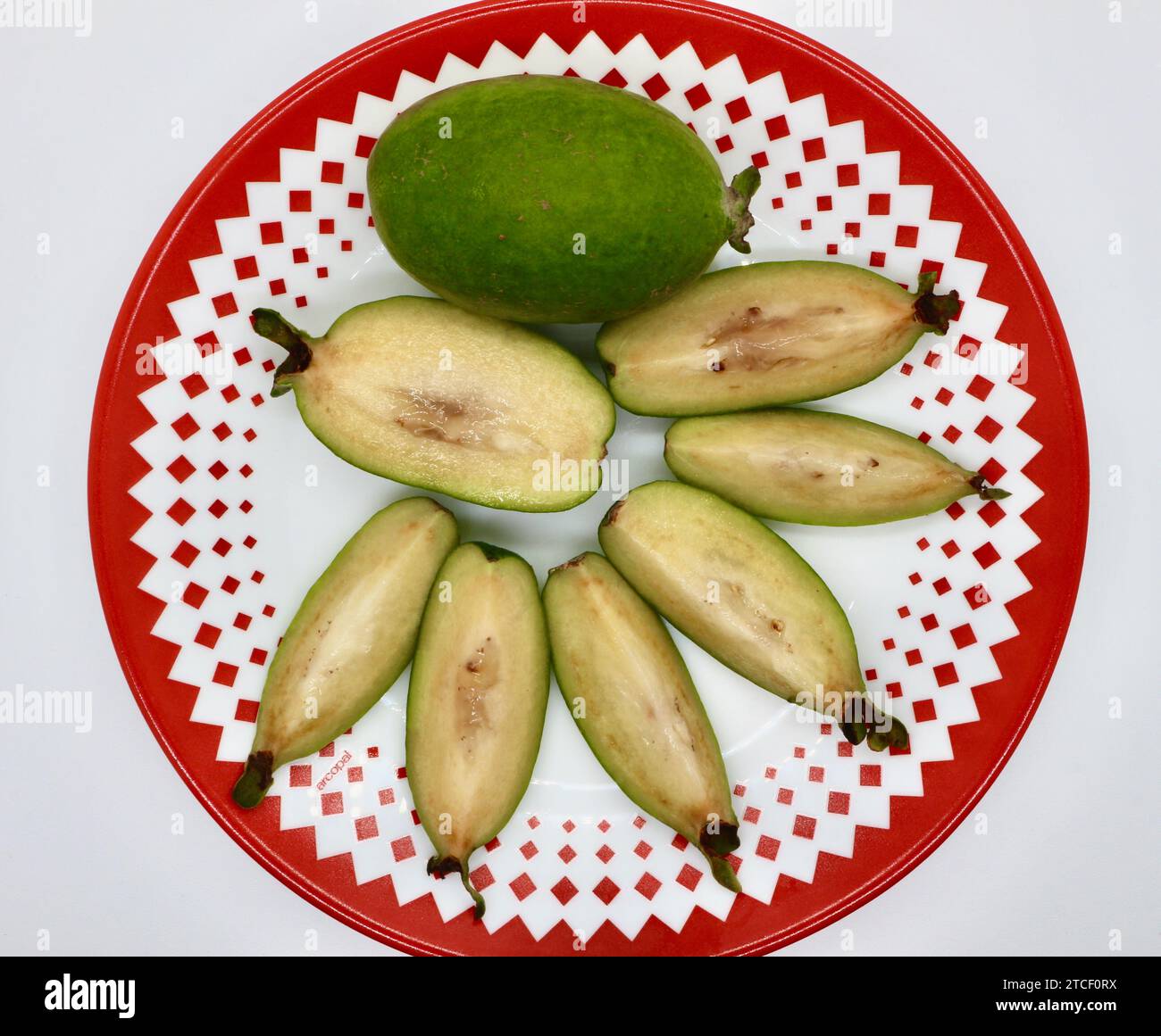 Weiße Guavafrucht Psidium Guajava ganz und geschnitten auf einem rot-weiß gemusterten Teller von oben nach unten Stockfoto