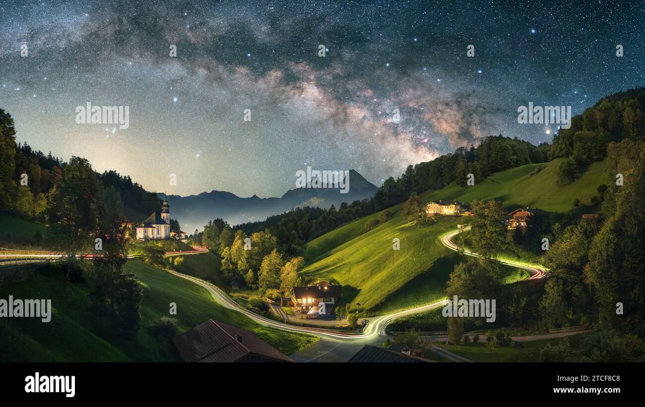 Atemberaubende Nachtaufnahme der ikonischen Landschaft in den Alpen, einem idyllischen Dorf mit einer kleinen Kirche und einer gewundenen Straße auf den Hügeln, die mit Lichtwegen beleuchtet sind Stockfoto