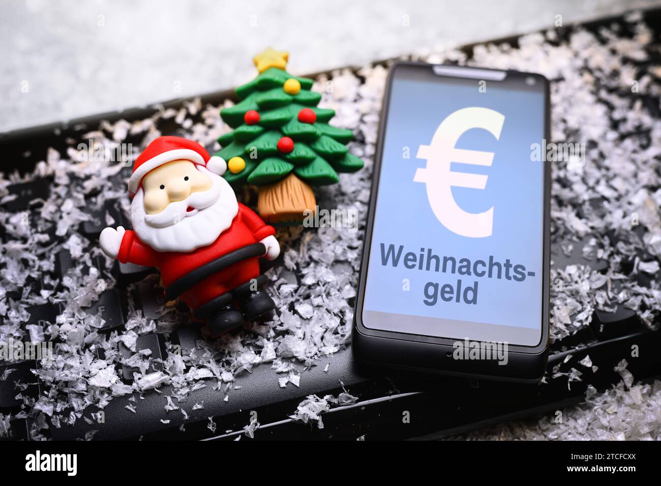 FOTOMONTAGE, Smartphone mit Aufschrift Weihnachtsgeld, Weihnachtsmannfigur und Tannenbaum auf Computertastatur *** FOTOMONTAGE, Smartphone mit Aufschrift Weihnachtsbonus, Weihnachtsmannfigur und Weihnachtsbaum auf Computertastatur Stockfoto