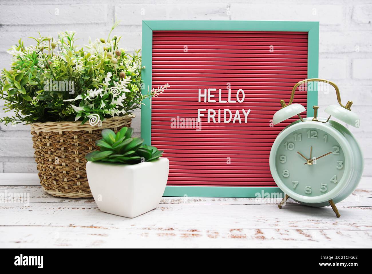 Hallo Freitag Text auf der Brieftafel mit Alarmtafel und künstlicher Pflanzendekoration Stockfoto