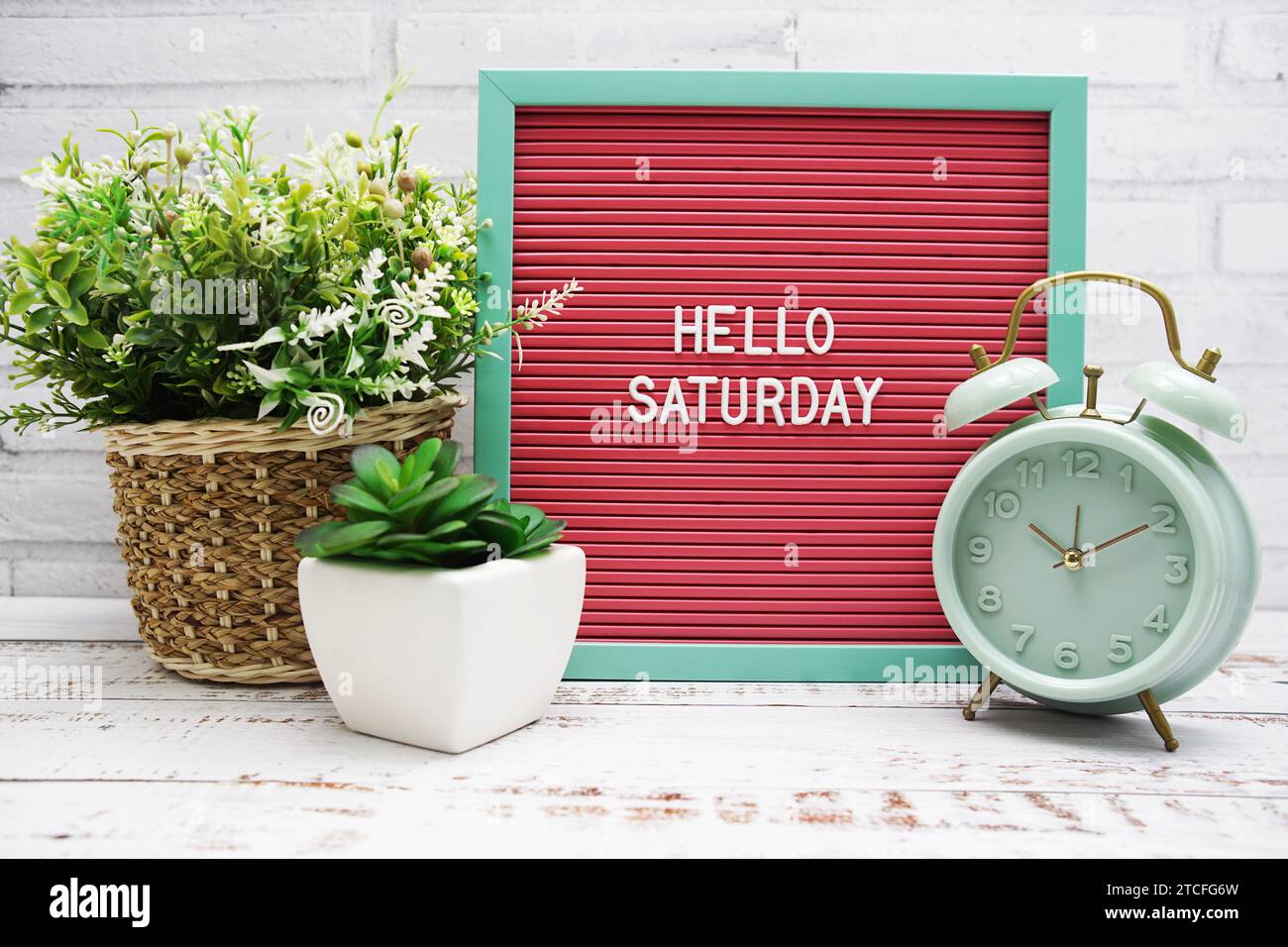 Hallo Samstag Text auf der Brieftafel mit Alarmtafel und künstlicher Pflanzendekoration Stockfoto