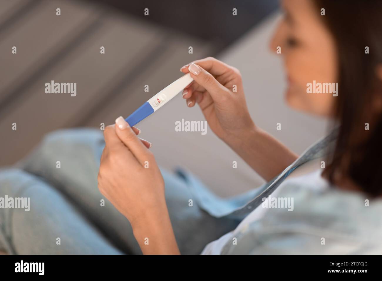 Lächelnde schwangere Dame hält positiven Schwangerschaftstest sitzend drinnen, abgeschnitten Stockfoto