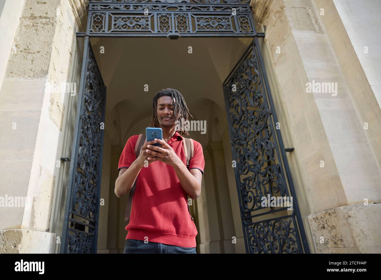 Männlicher Student, der Nachrichten oder soziale Medien auf einem Mobiltelefon außerhalb des Universitätsgebäudes in Oxford UK abfragt Stockfoto