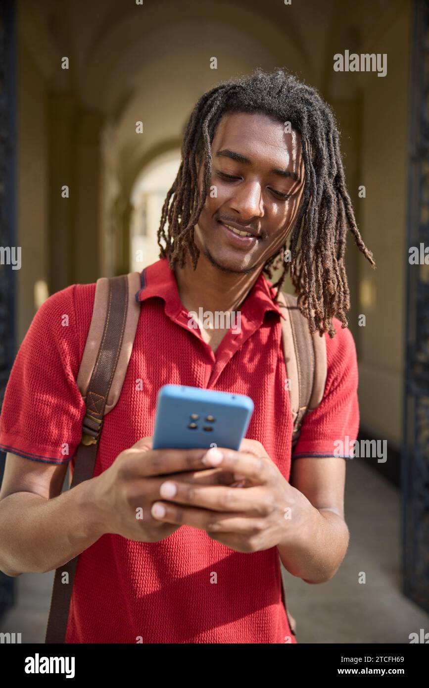 Männlicher Student, der Nachrichten oder soziale Medien auf einem Mobiltelefon außerhalb des Universitätsgebäudes in Oxford UK abfragt Stockfoto