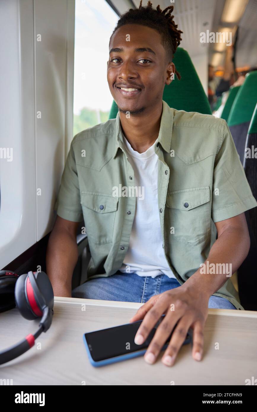 Porträt Eines Jungen Mannes, Der Mit Schnurlosen Kopfhörern Und Mobiltelefon Im Zug Zur Arbeit Fährt Stockfoto