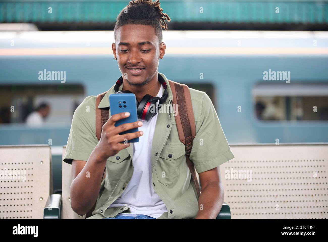 Junger Mann, Der Im Zug Zur Arbeit Pendelt, Sitzt Auf Der Plattform Und Schaut Auf Ein Mobiltelefon Für Reiseinformationen Oder Soziale Medien Stockfoto