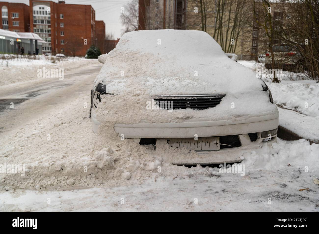 Ein Auto, das nach dem Schneeräumungsprozess auf einer Winterstraße im Schnee vergraben ist. Das Fahrzeug ist fast vollständig abgedeckt, nur kleine Teile sind sichtbar, hochgradig Stockfoto