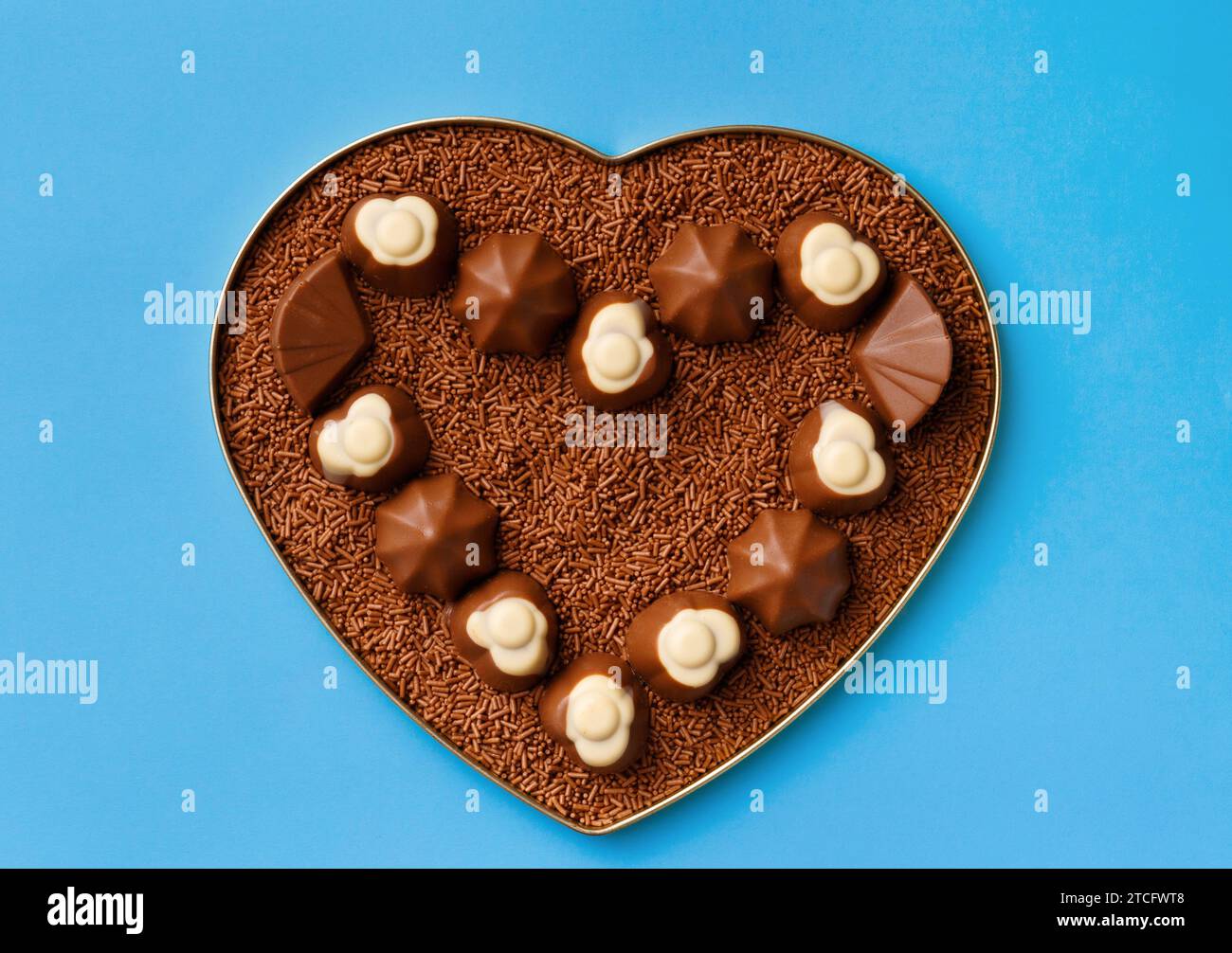Herzförmige Schachtel mit Schokolade und Schokoladenchips auf blauem Hintergrund, Blick von oben. Postkarte, Vorlage für Valentinstag. Stockfoto