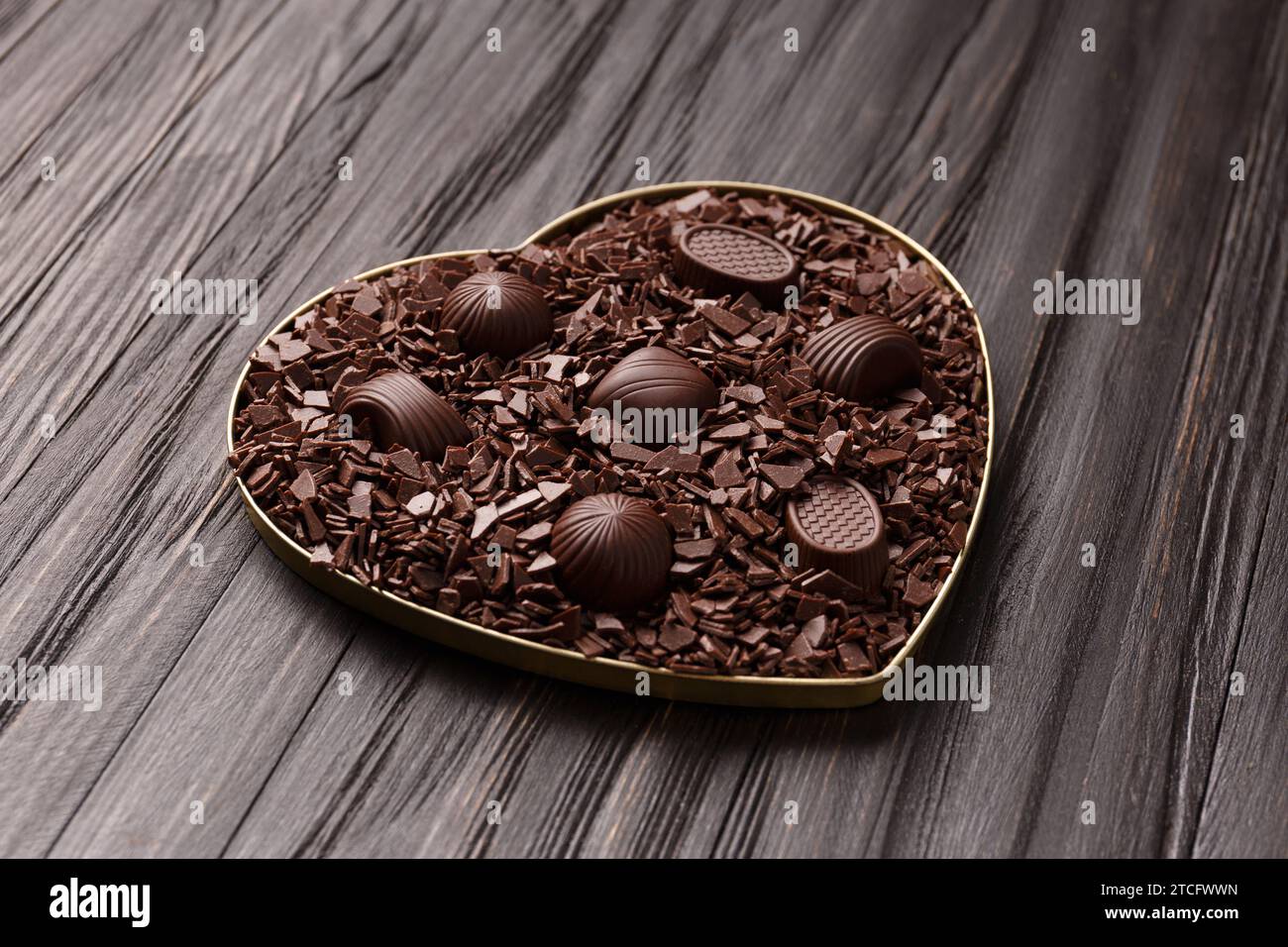 Schokoladenbonbons in Schokoladenstückchen in einer herzförmigen Schachtel auf einem dunklen Holzhintergrund mit Blick auf den Valentinstag. Stockfoto