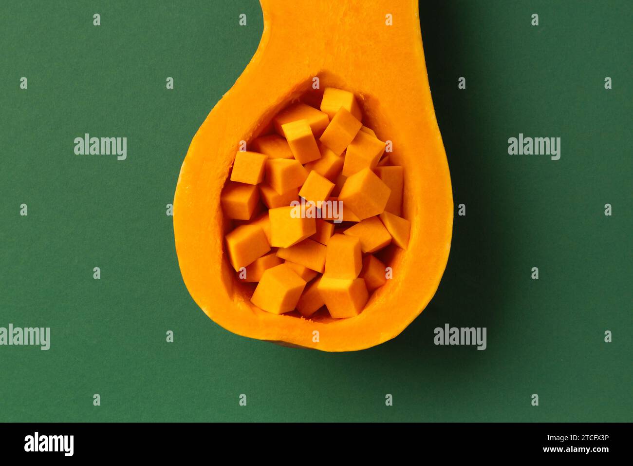 Die Hälfte eines orangen süßen Butternusskürbis und gewürfelten Kürbis innen auf grünem Hintergrund, Draufsicht. Gesundes Gemüse, Vegetarismus. Stockfoto