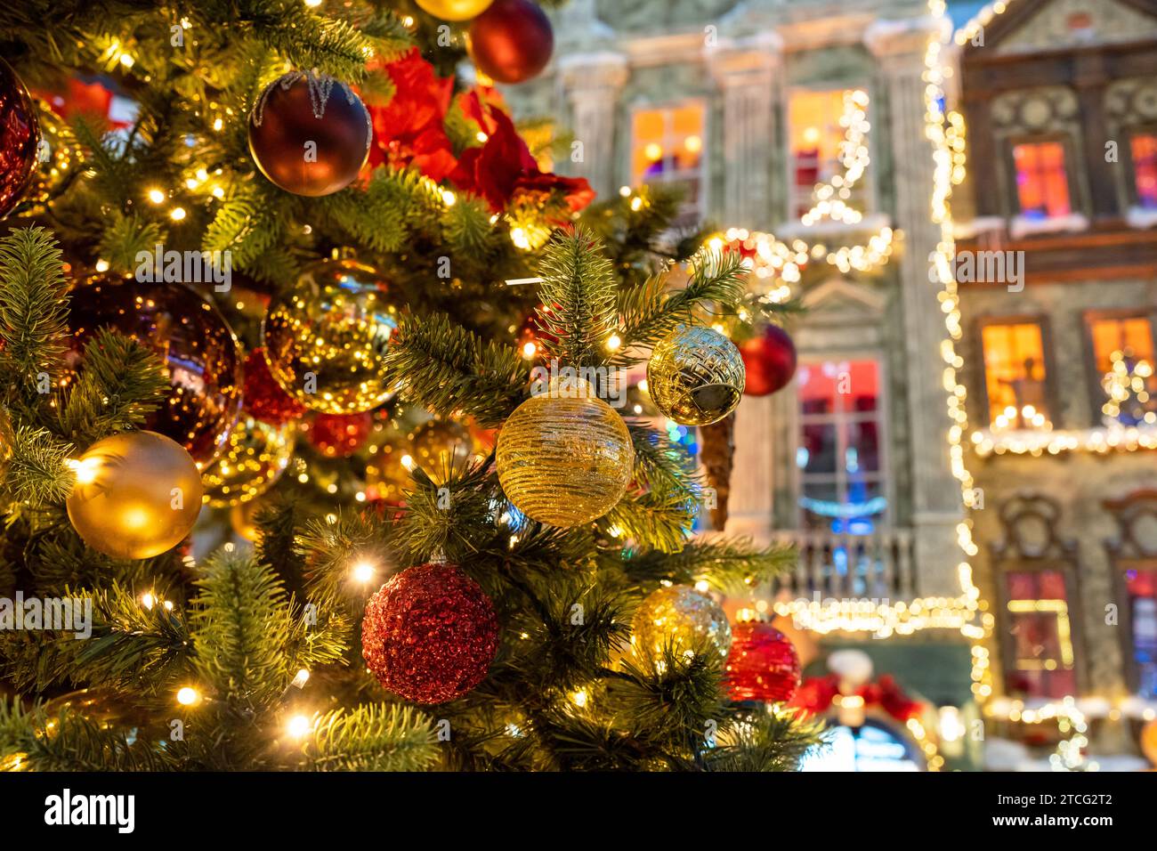 Nahaufnahme des festlich dekorierten Weihnachtsbaums im Freien mit bunten Kugeln auf einem schimmernden, glitzernden Feenhintergrund. Defokussierte Nachtstraße, Girlande Stockfoto