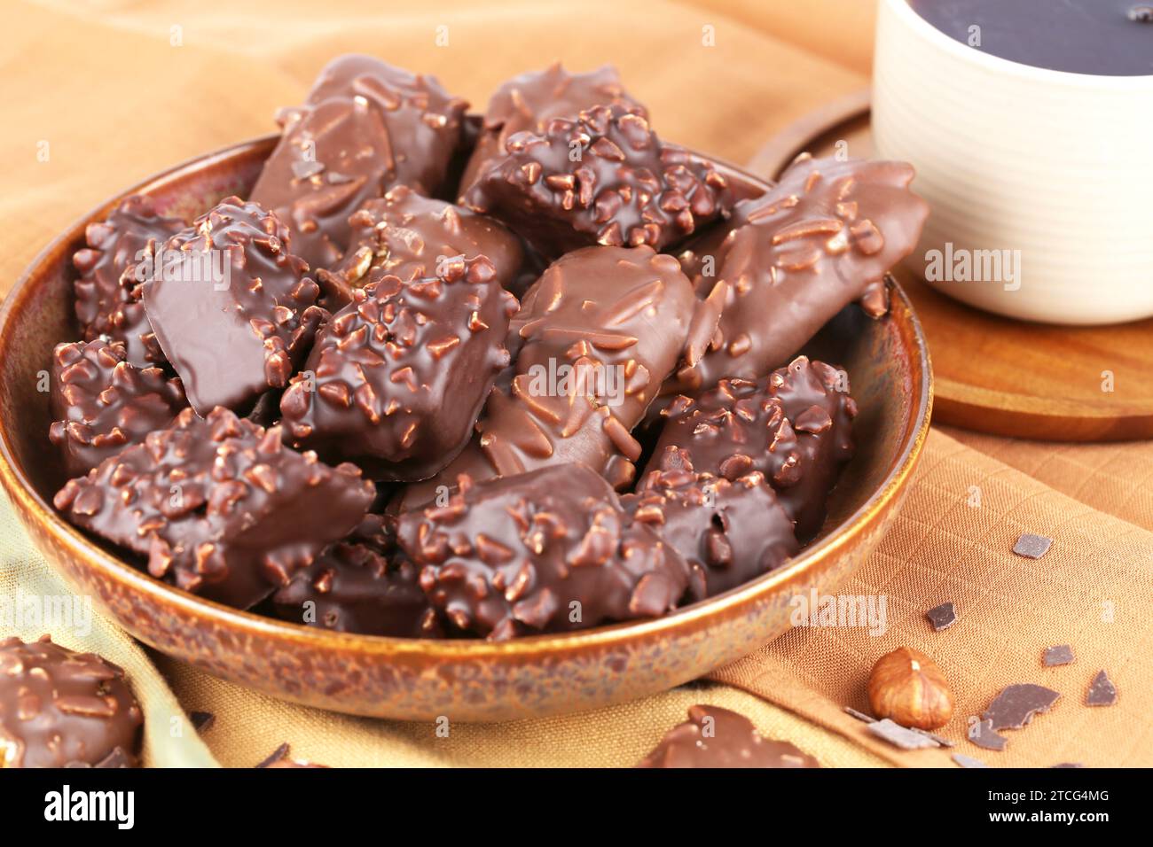 Schokolade mit Haselnüssen in Keramikschale und Tasse Tee auf dem braunen Stoffhintergrund. Stockfoto