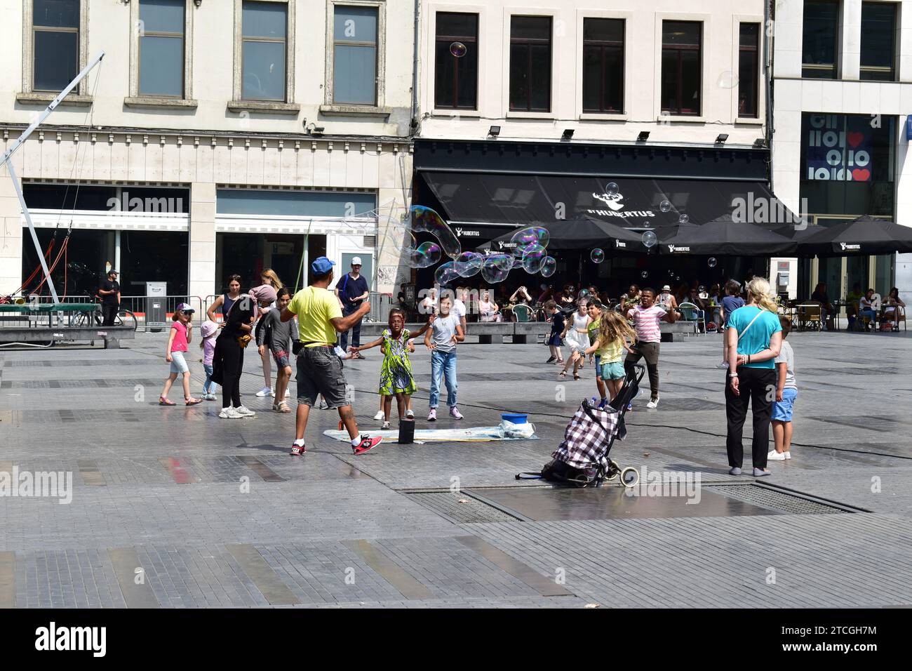 Mann in gelbem T-Shirt, der große Seifenblasen erzeugt, um kleine Kinder auf dem Munt (Punt) Platz im Stadtzentrum von Brüssel zu unterhalten Stockfoto