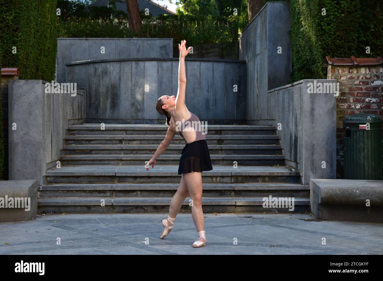 Eine junge Frau in lila Oberteil und schwarzem Rock, die vor der Treppe eine Ballettposition auf einer Steinoberfläche spielt Stockfoto