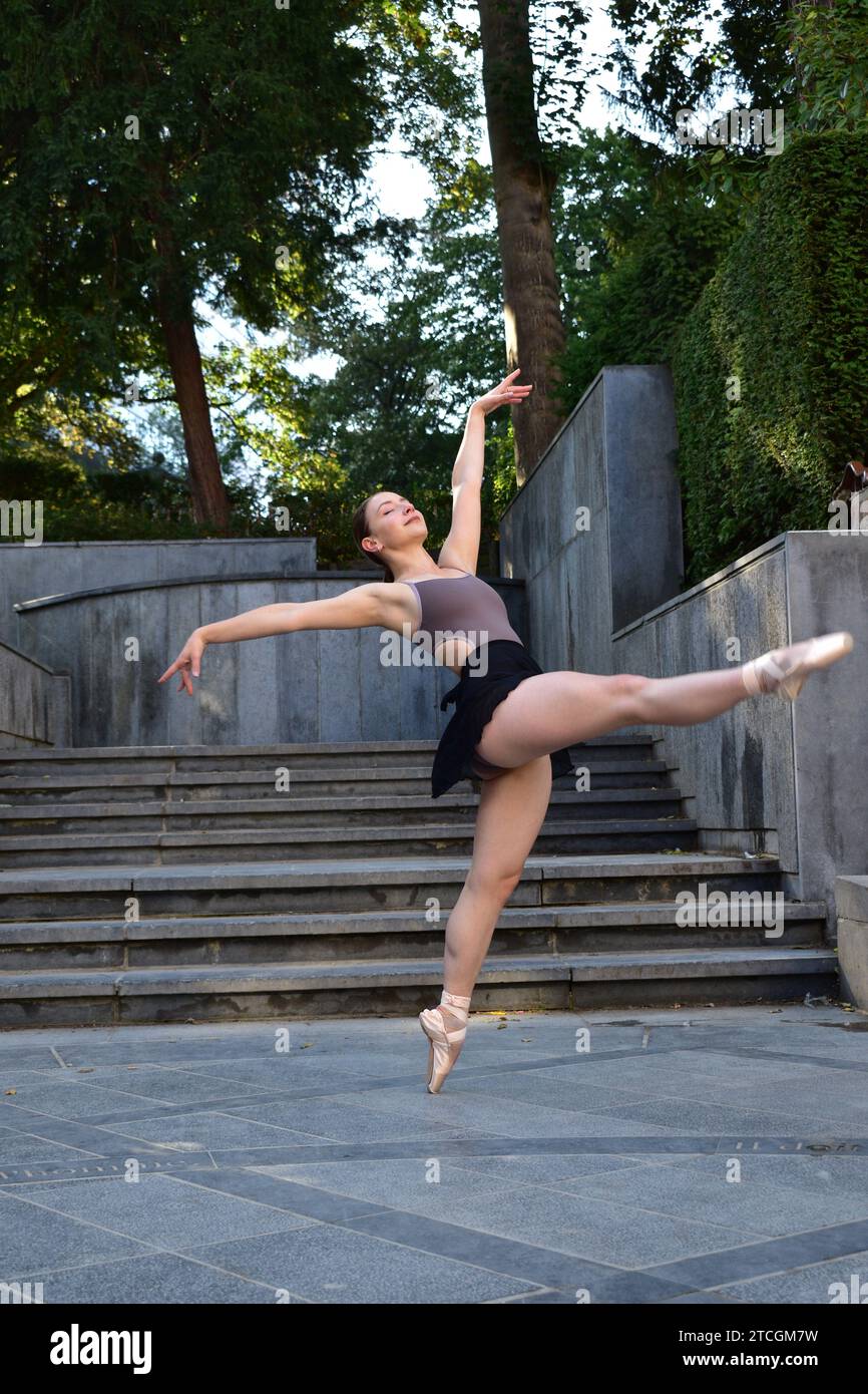 Eine junge Frau in lila Oberteil und schwarzem Rock, die vor der Treppe eine Ballettposition auf einer Steinoberfläche spielt Stockfoto