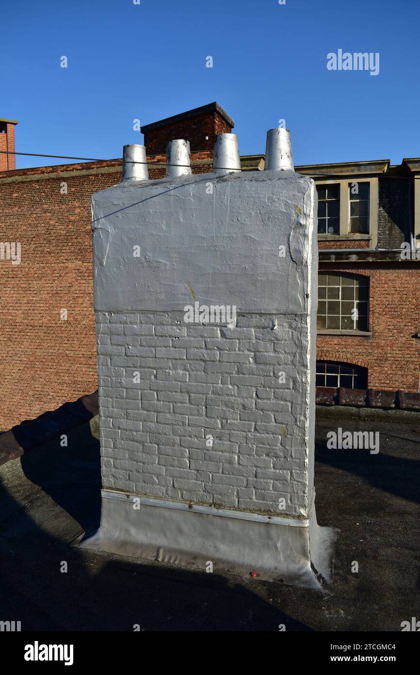 Ein rechteckiger Ziegel- und Betonschornstein mit 4 Rauchauslässen, mit Silberfarbe bemalt, mit Ziegelbau und blauem Himmel im Hintergrund Stockfoto