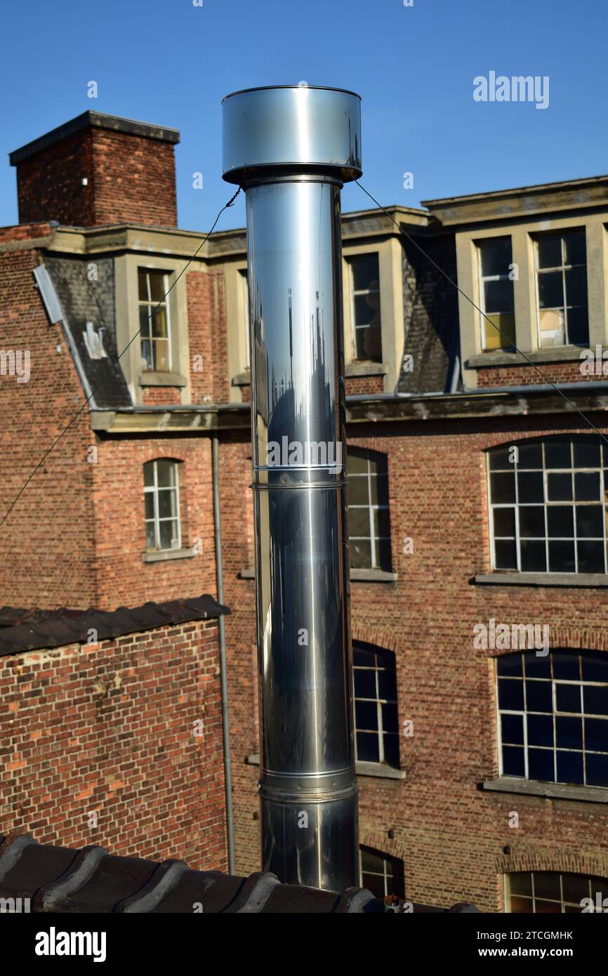 Nahaufnahme einer Edelstahl-Chrom-Metall-Lüftungsöffnung, die als Schornstein auf einem Dach mit Ziegelbau im Hintergrund verwendet wird Stockfoto