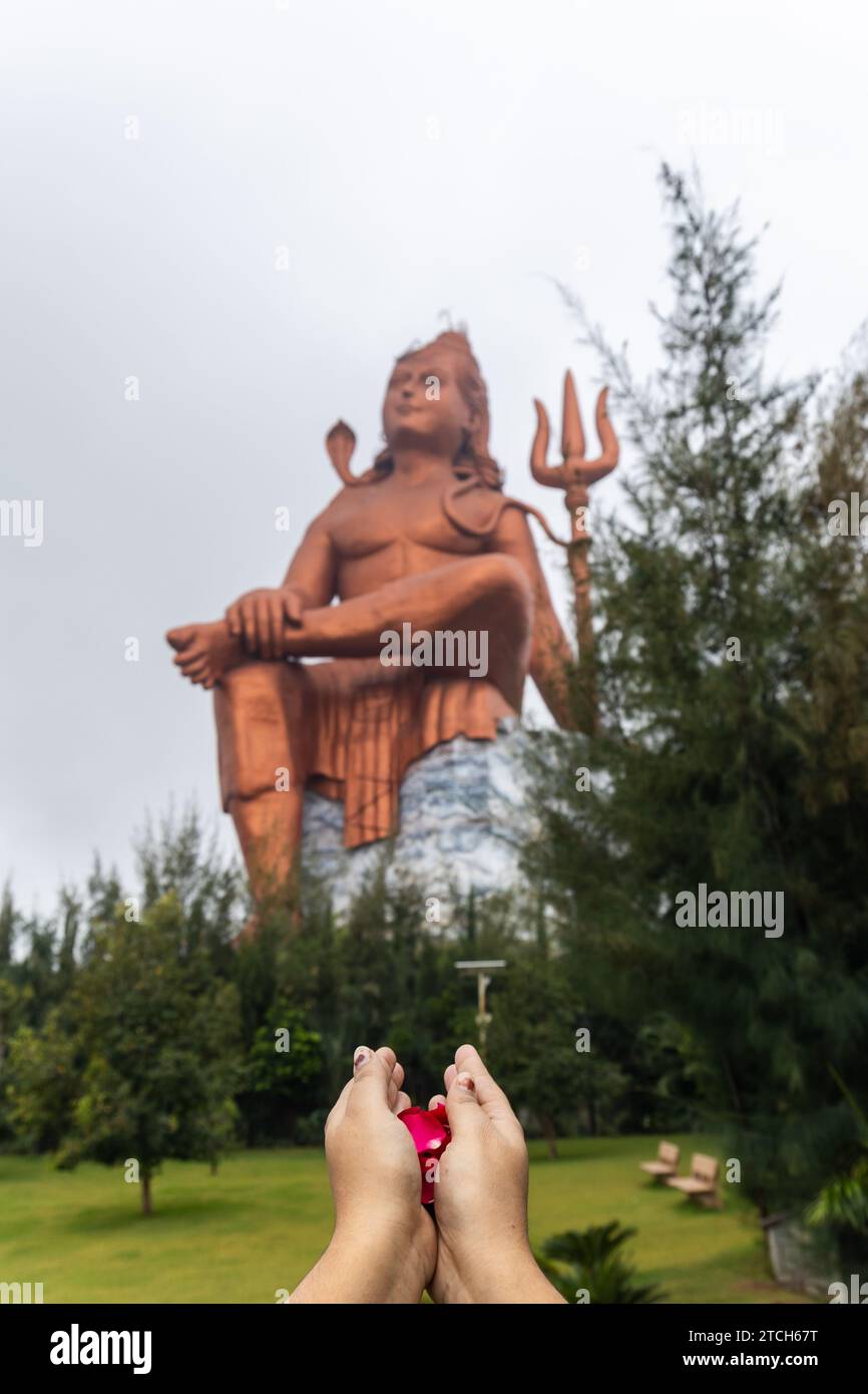 Die geweihte Hand mit Blumen und die verschwommene Statue des hindugottes shiva am Morgen wird an der Glaubensstatue oder Vishwas Swaroopam nathd aufgenommen Stockfoto