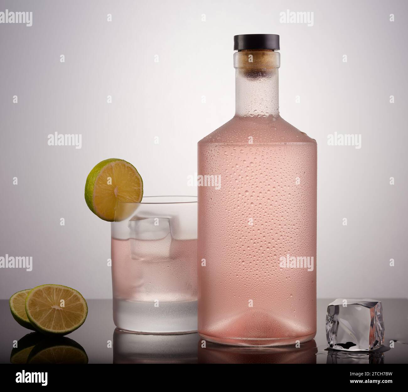 Pinke Gin-Flasche und ein Glas rosa Gin mit Eis und Limette garniert, mit einem kühlen Farbverlauf Hintergrund. Stockfoto