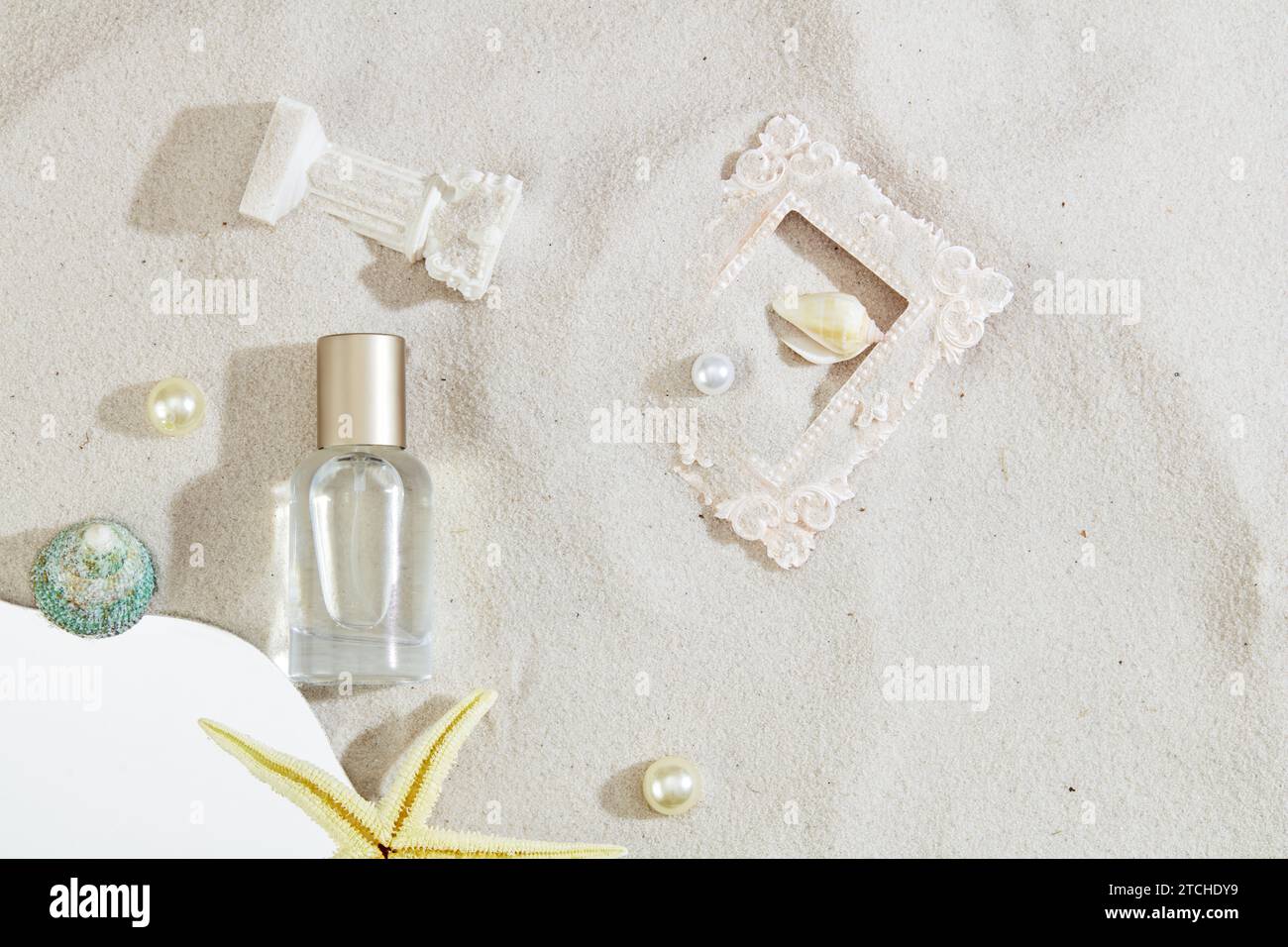 Eine Parfümflasche ohne Marke, die mit Muscheln, Perlen und Ornamenten auf sandigem Hintergrund verziert ist. Ein frisches, lebendiges Sommererlebnis. Draufsicht elegan Stockfoto