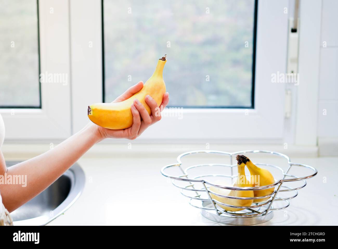 Frau Hand hält Banane, Snack und gesundes Konzept. Selektiver Fokus auf Händen mit verschwommenem Hintergrund und Kopierraum Stockfoto