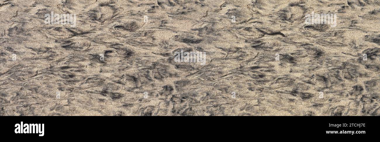 Abstraktes Muster aus schwarzem und braunem Sand auf einem flachen Boden am Strand Stockfoto