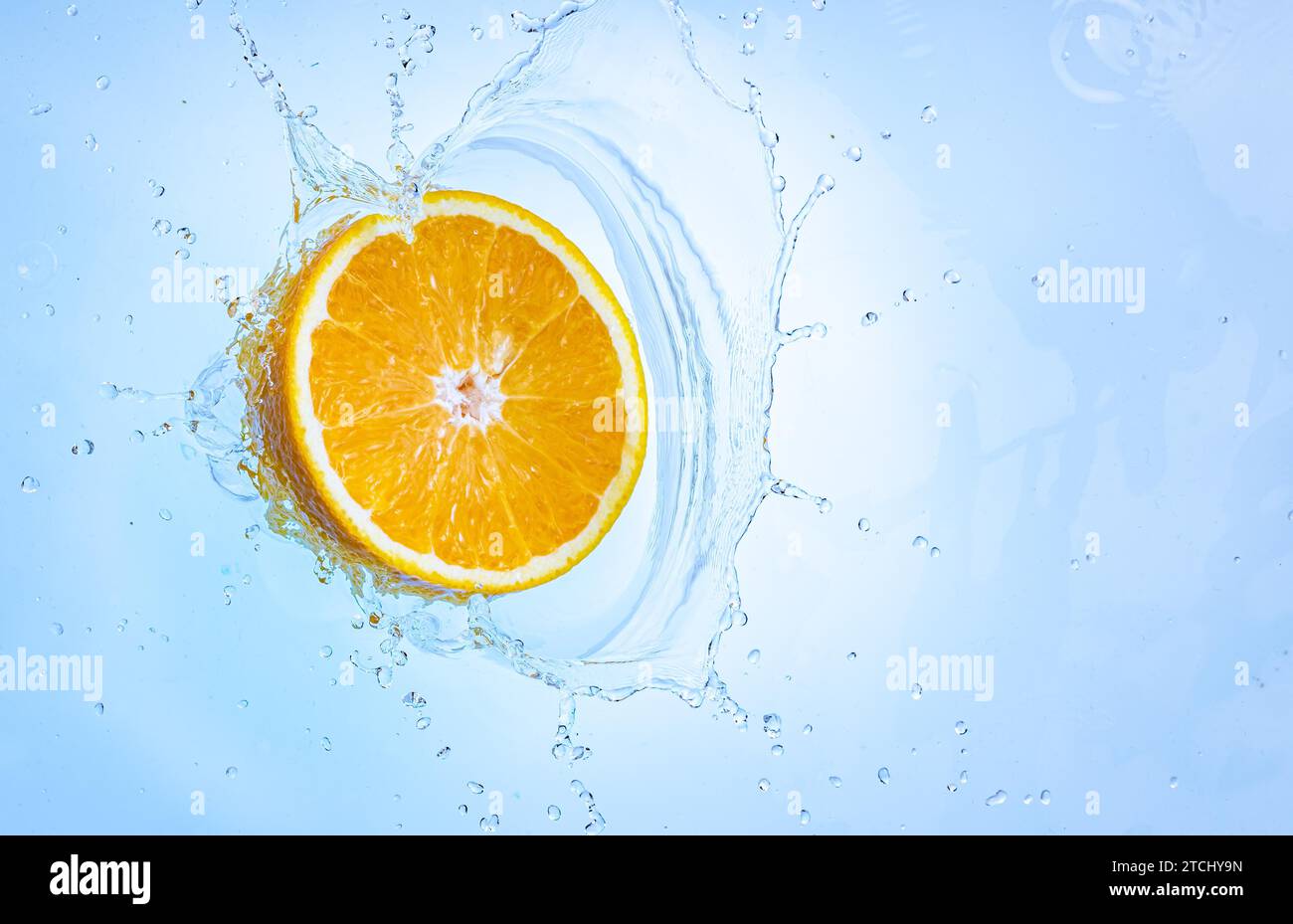 Frisch reife Hälfte Orange spritzt in klares Wasser, isoliert auf hellblauem Hintergrund. Gesundheitsnahrungskonzept Stockfoto