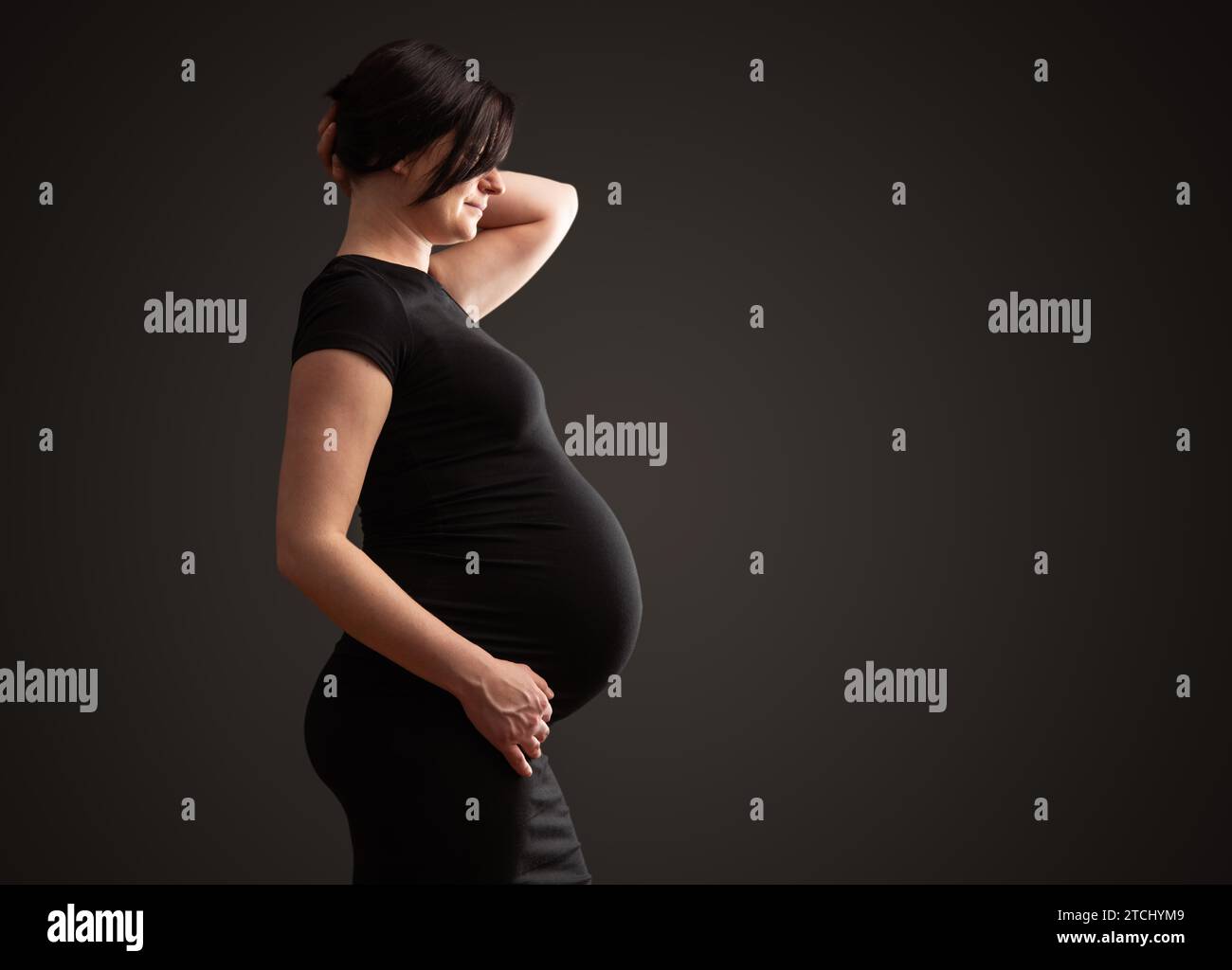 Junge schöne schwangere Frau mit dunklem Haar vor dunklem Hintergrund Stockfoto