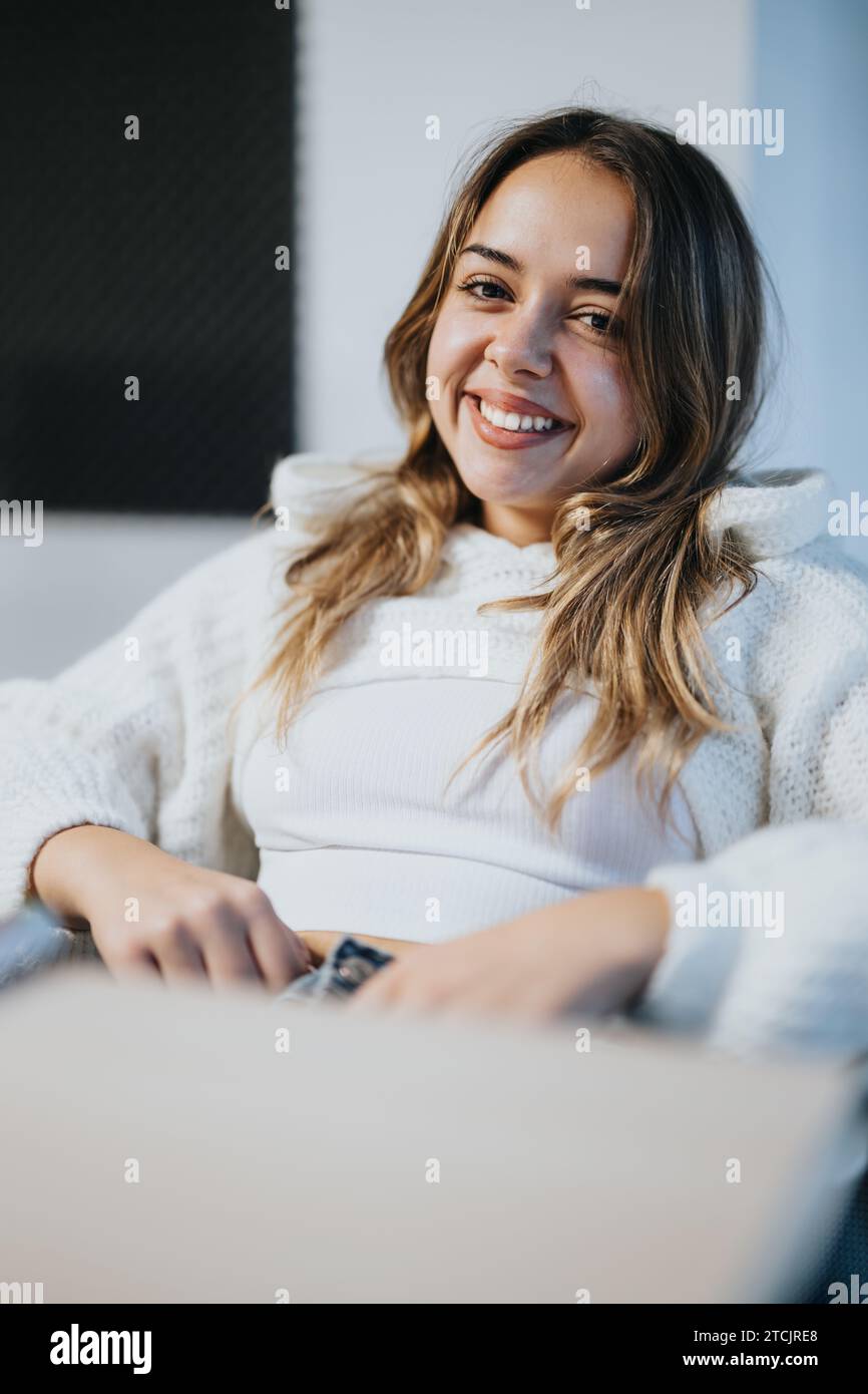 Nette, junge, weibliche Angestellte, die auf die Kamera blickte und lächelte, während sie auf einem Stuhl im Büro saß. Stockfoto