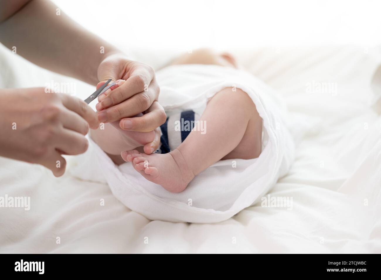 Mutterhände schneiden die Zehennägel des Neugeborenen mit einer Schere Stockfoto