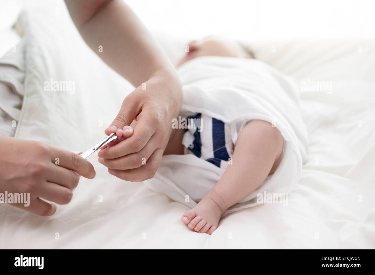 Mutterhände schneiden die Zehennägel des Neugeborenen mit einer Schere Stockfoto