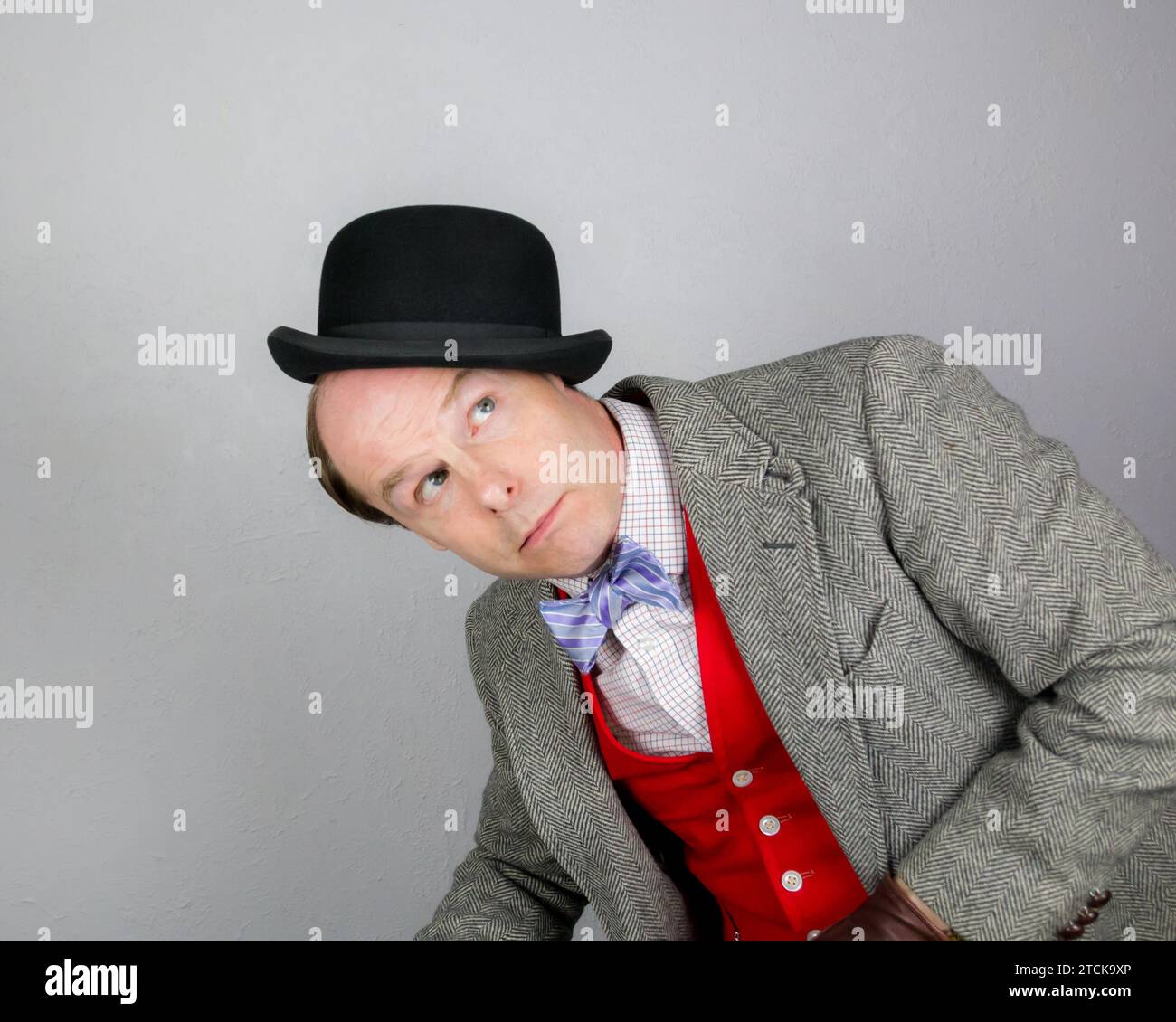 Porträt eines britischen Charakters in Tweed-Anzug und roter Weste, der einen Bowler-Hut auf seinem Kopf ausbalanciert. Konzept des Vintage Vaudeville Comic Schauspielers. Stockfoto