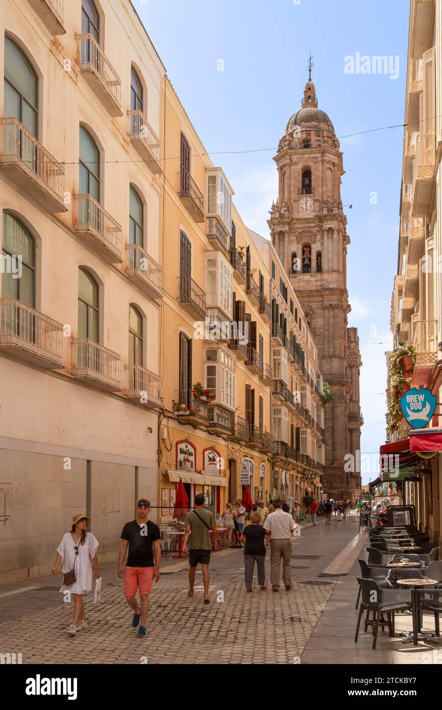 Die Menschen laufen durch eine enge Einkaufsstraße in der Stadt Málaga mit dem Domturm im Hintergrund. Stockfoto