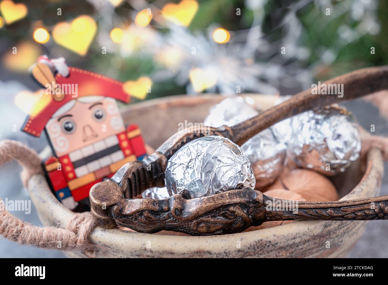 Dekorierte Nüsse und Nussknacker. Nussknacker Aus Holz. Hölzernes Weihnachtsspielzeug mit Nüssen in der Schale und silbernem Papier auf weihnachtlichem Hintergrund. Stockfoto