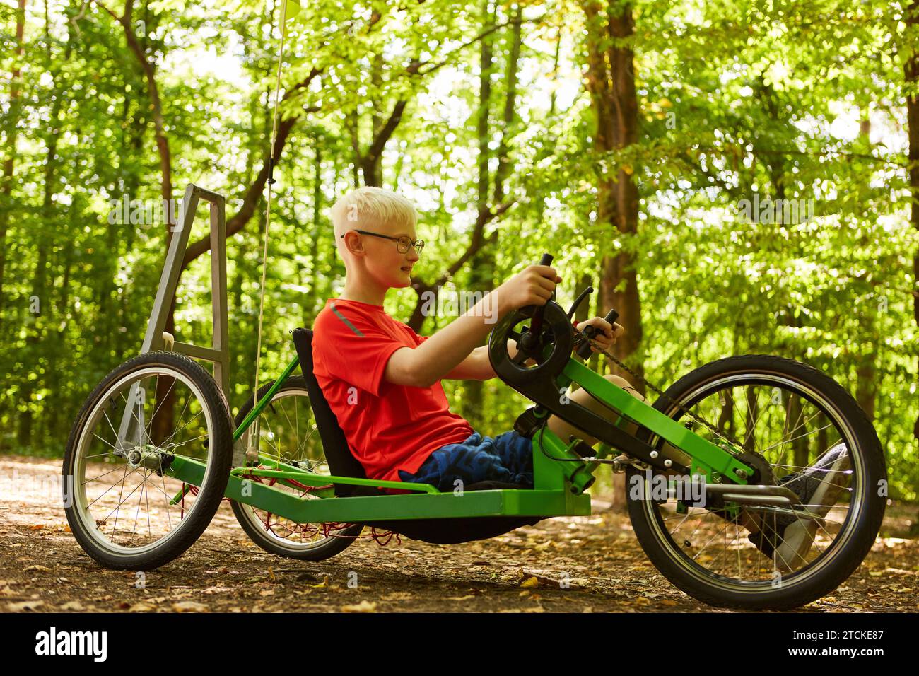 Die ganze Länge eines behinderten Jungen, der auf dem Liegerad auf dem Fußweg im Wald fährt Stockfoto