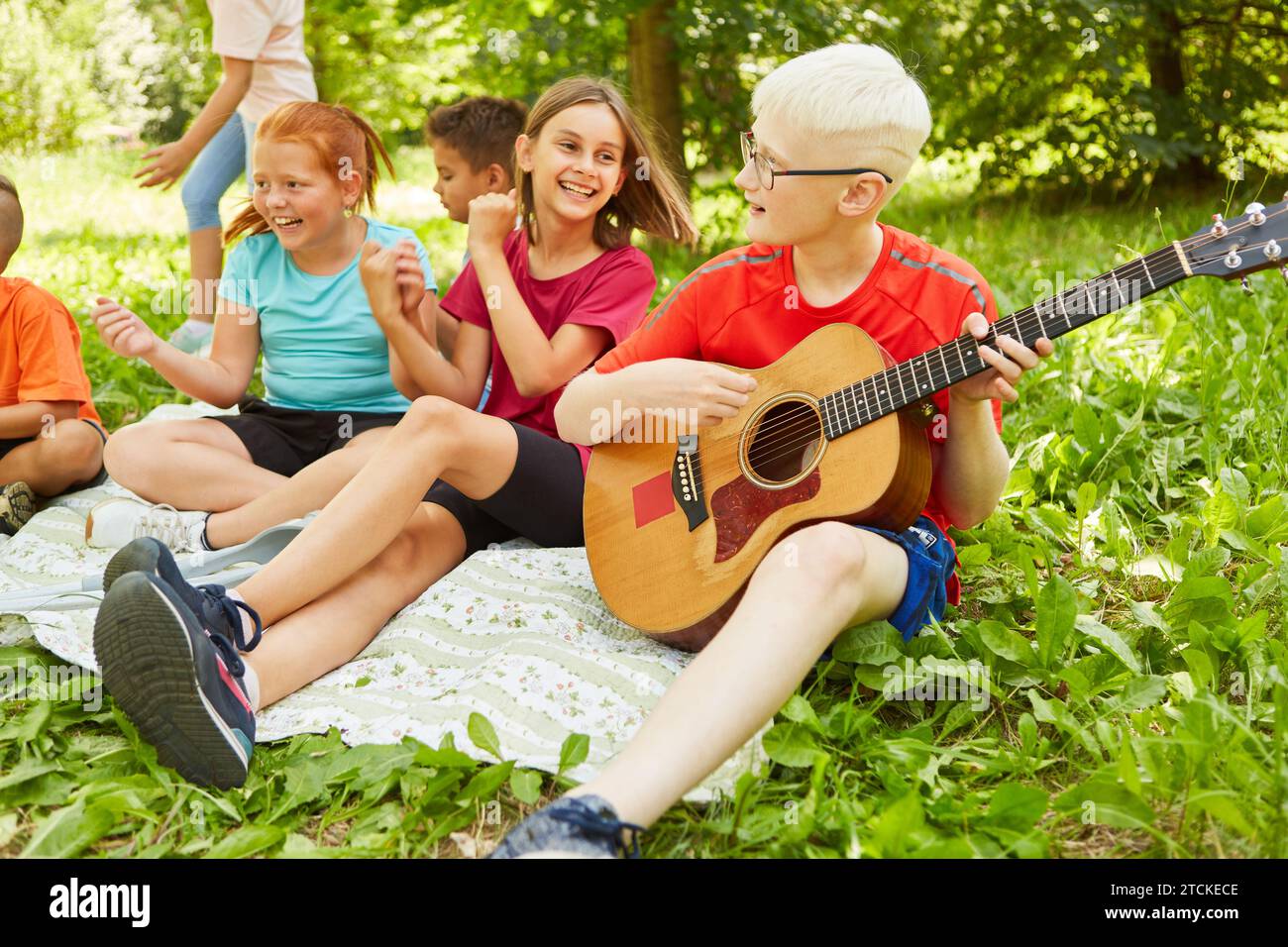 Behinderter Junge, der Gitarre spielt, während er sich mit Freunden während des Picknicks im Park auf eine Decke setzt Stockfoto