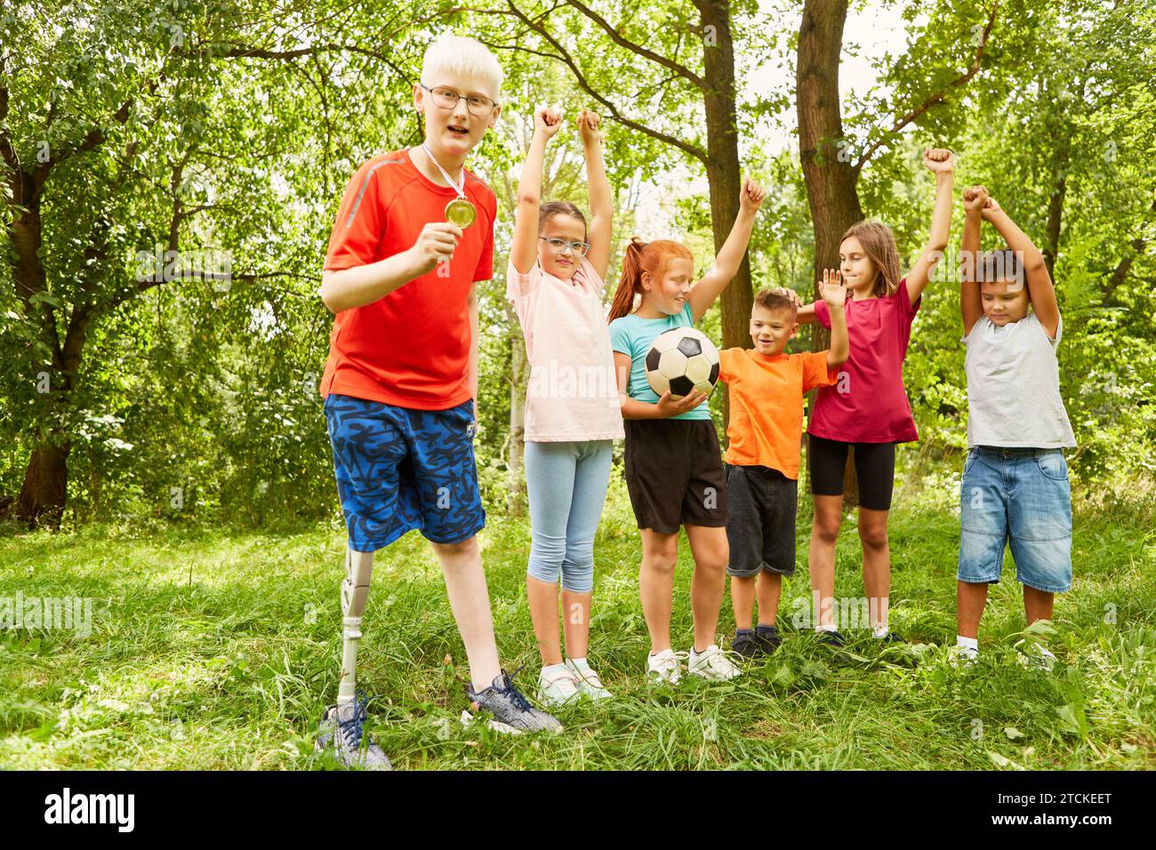 Behinderter Junge mit Medaille, während er mit Freunden steht und den Sieg im Park feiert Stockfoto