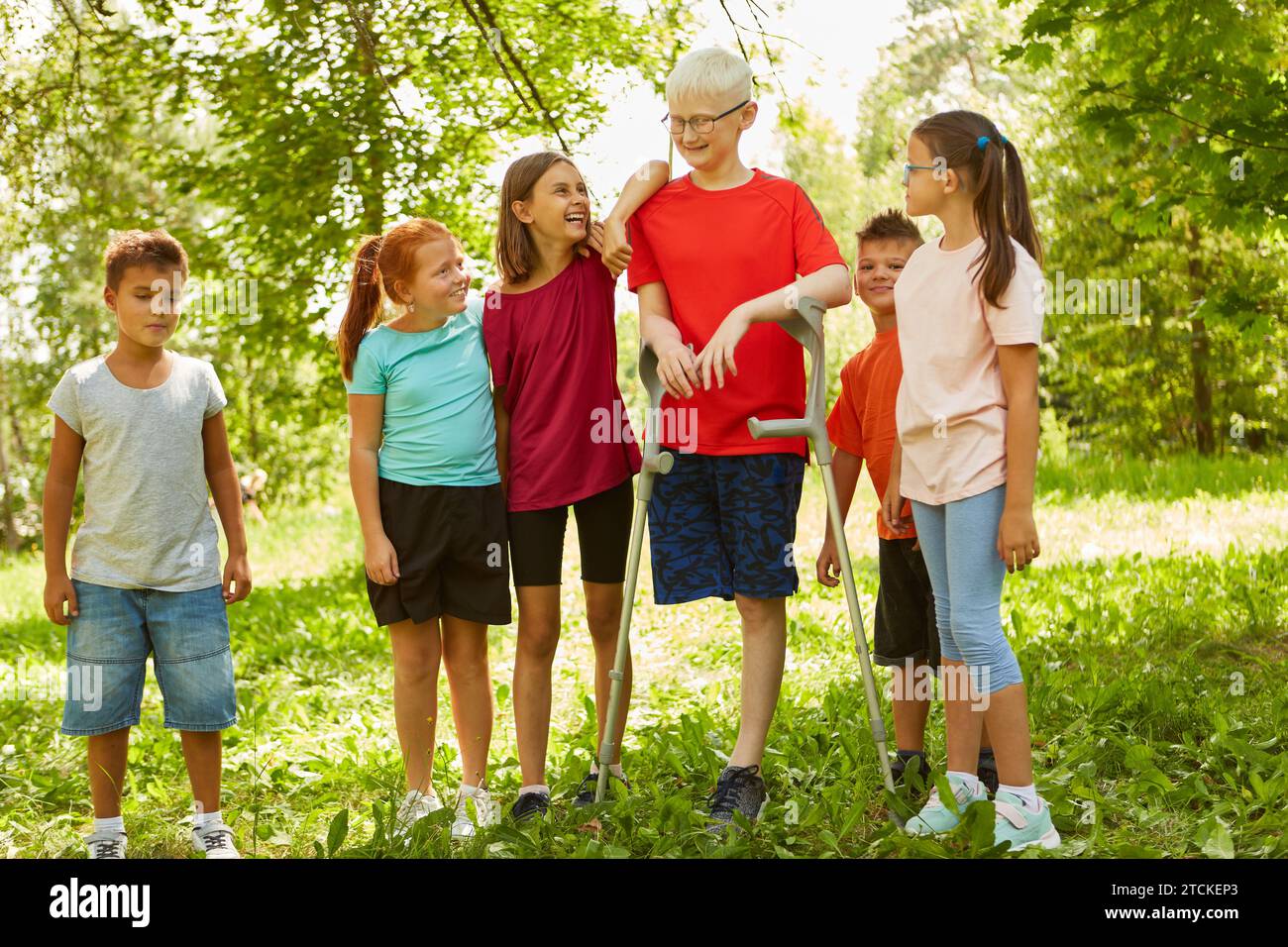 Lächelnde männliche und weibliche Freunde stehen mit einem behinderten Jungen im Park Stockfoto