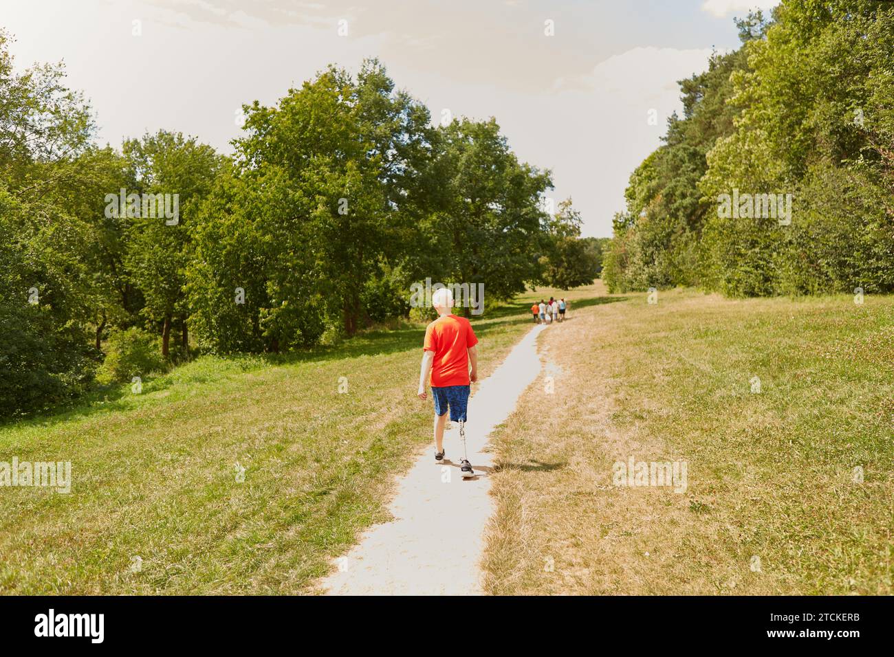 Rückansicht auf voller Länge eines behinderten Jungen, der auf dem Fußweg im Park läuft Stockfoto