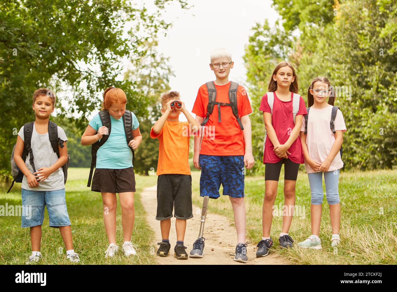 Gruppe von Kindern mit Rucksäcken, die im Sommer auf einem Wanderweg mit behindertem Jungen mit prothetischem Bein laufen Stockfoto