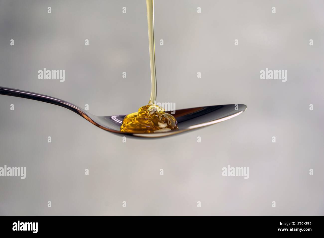 Honig in einen Löffel gießen, isoliert auf grauem Hintergrund, Lebensmittelillustration Stockfoto